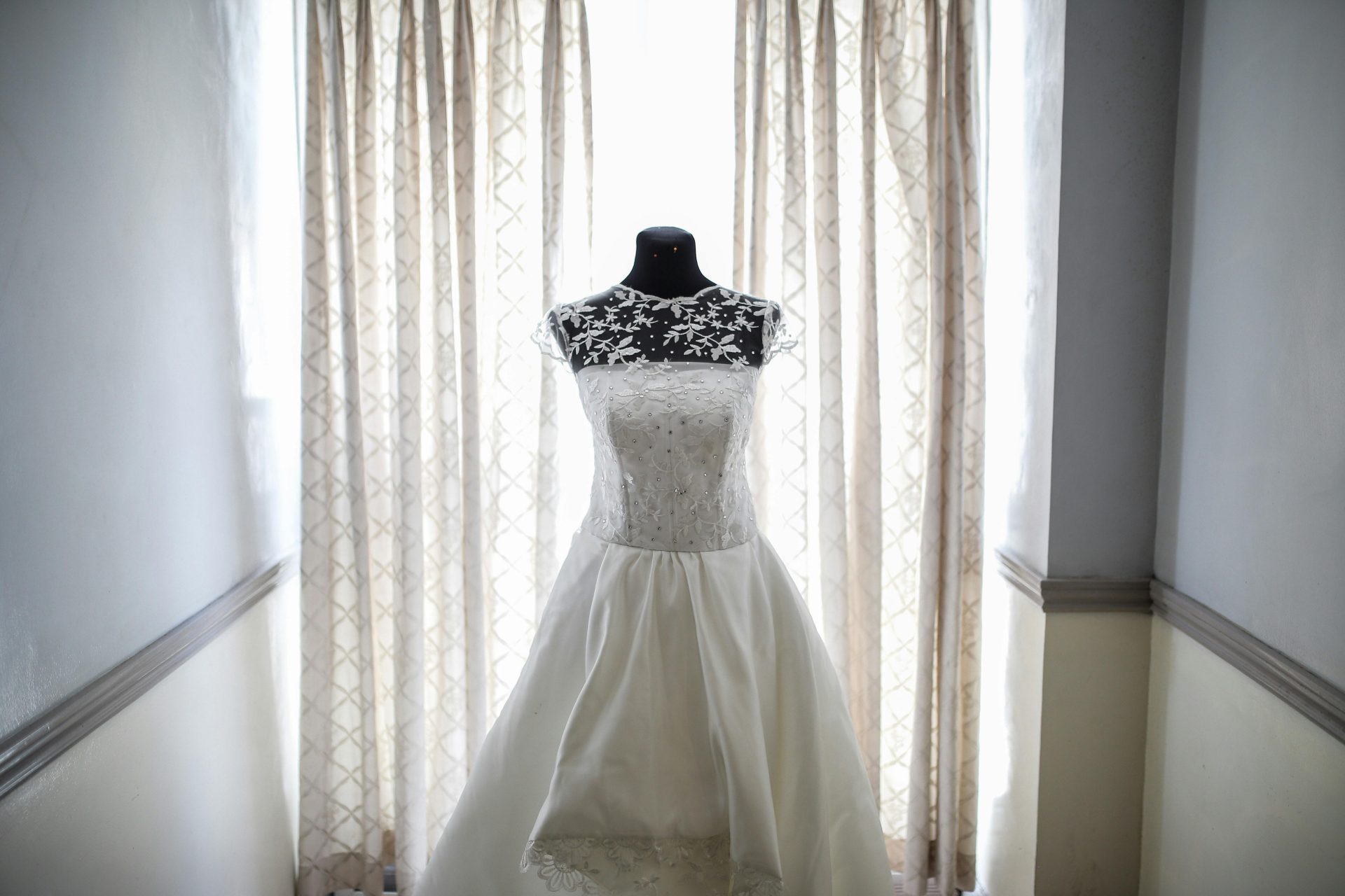 A beautiful bridal gown displayed on a mannequin, illuminated by natural light from a window.